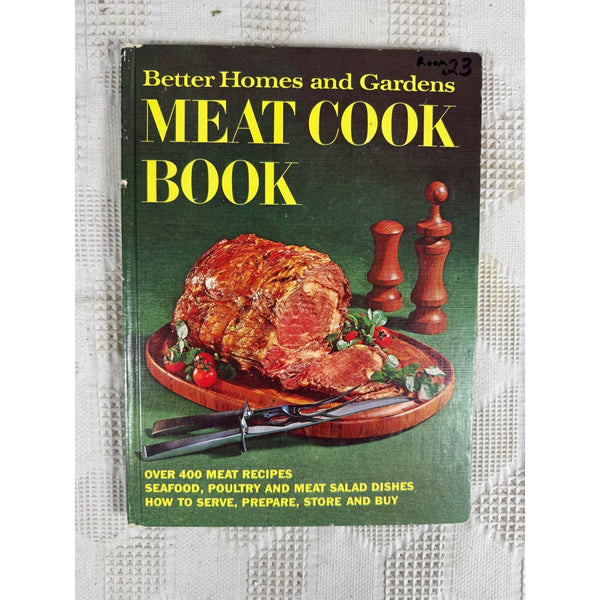 Better Homes and Gardens 1968 Meat Cook Book Over 400 Recipes Fourth Edition. A vintage Better Homes and Gardens Meat Cook Book with a dark green cover featuring a large sliced ham on a wooden platter, photographed on a textured white surface.